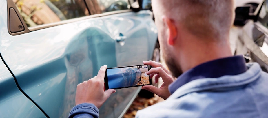 A man is taking pictures of a damaged car for his rideshare accident lawyer to look at.